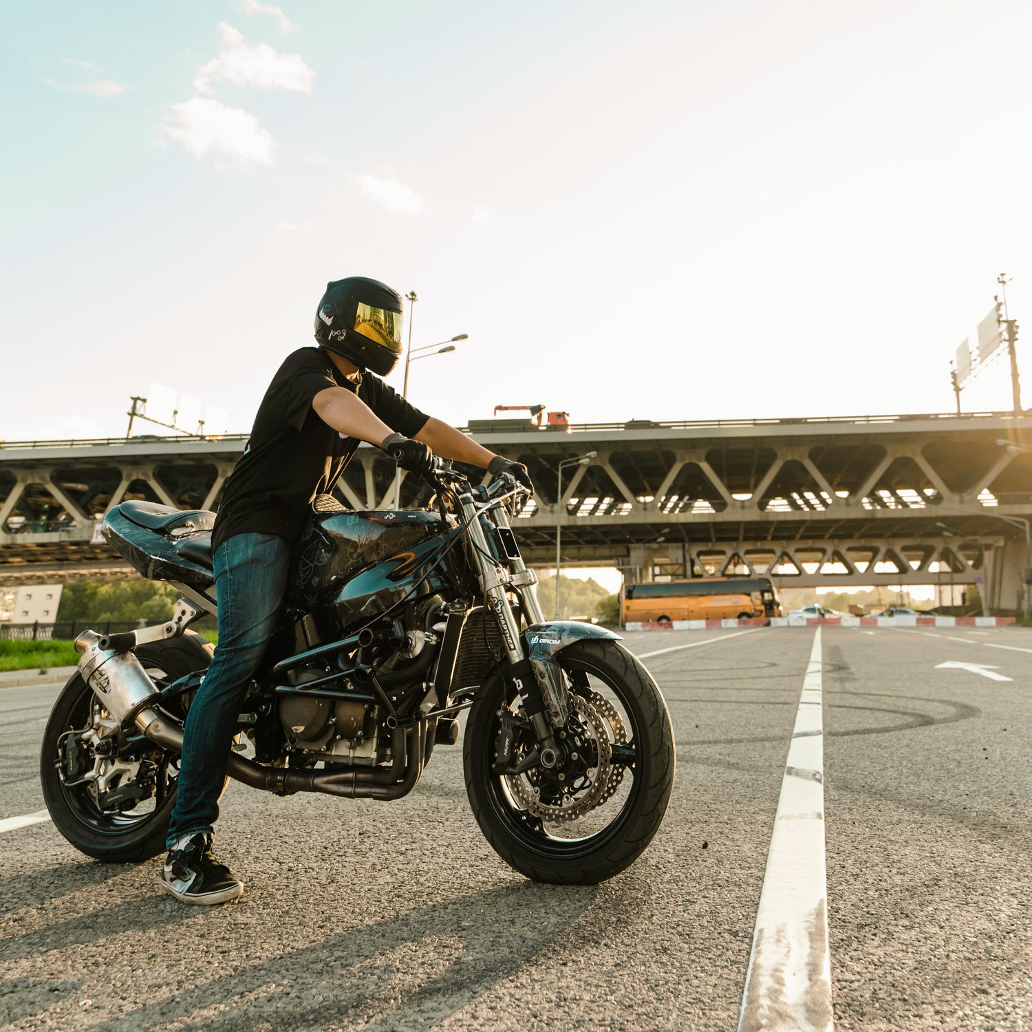 Man on two wheel sport motorcycle on gravel road wearing protective helmet and riding gear. Bridge in background cityscape
