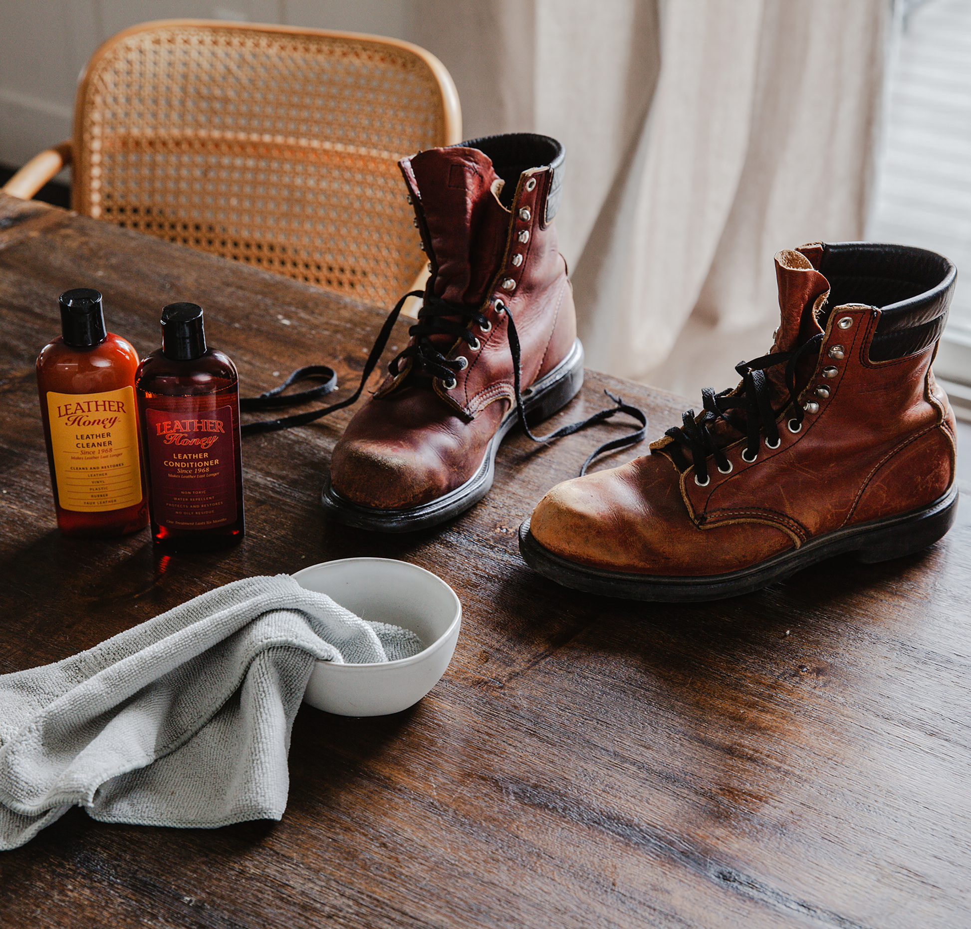 Brown leather boots on a wooden table with bottles of leather care products.