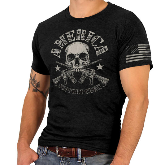 A man wearing a black short-sleeved t-shirt with a graphic print of a skull, crossed rifles, and the text 'AMERICA' and 'SUPPORT CREW'. There is an American flag on the left sleeve.