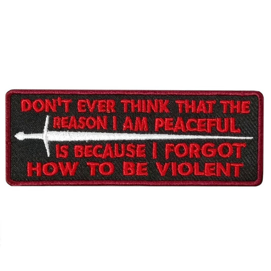 A black and red embroidered patch with the text 'DON'T EVER THINK THAT THE REASON I AM PEACEFUL IS BECAUSE I FORGOT HOW TO BE VIOLENT' along with an image of a sword.