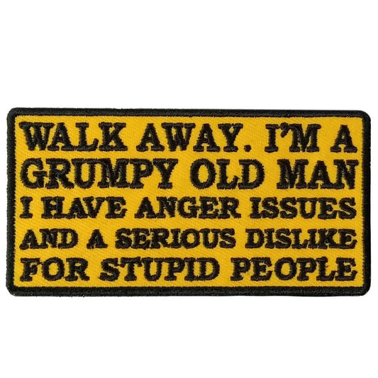 A rectangular yellow patch with black text that reads: 'WALK AWAY. I'M A GRUMPY OLD MAN I HAVE ANGER ISSUES AND A SERIOUS DISLIKE FOR STUPID PEOPLE'.