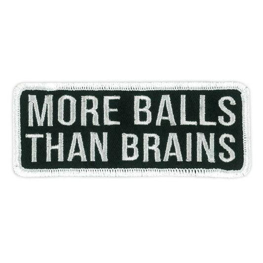 A rectangular black fabric patch with white embroidered text that reads 'MORE BALLS THAN BRAINS'.