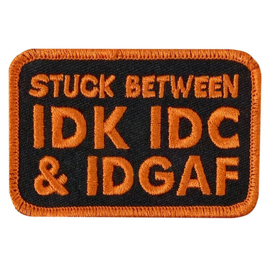 A black and orange embroidered patch with the text 'STUCK BETWEEN IDK IDC & IDGAF'.
